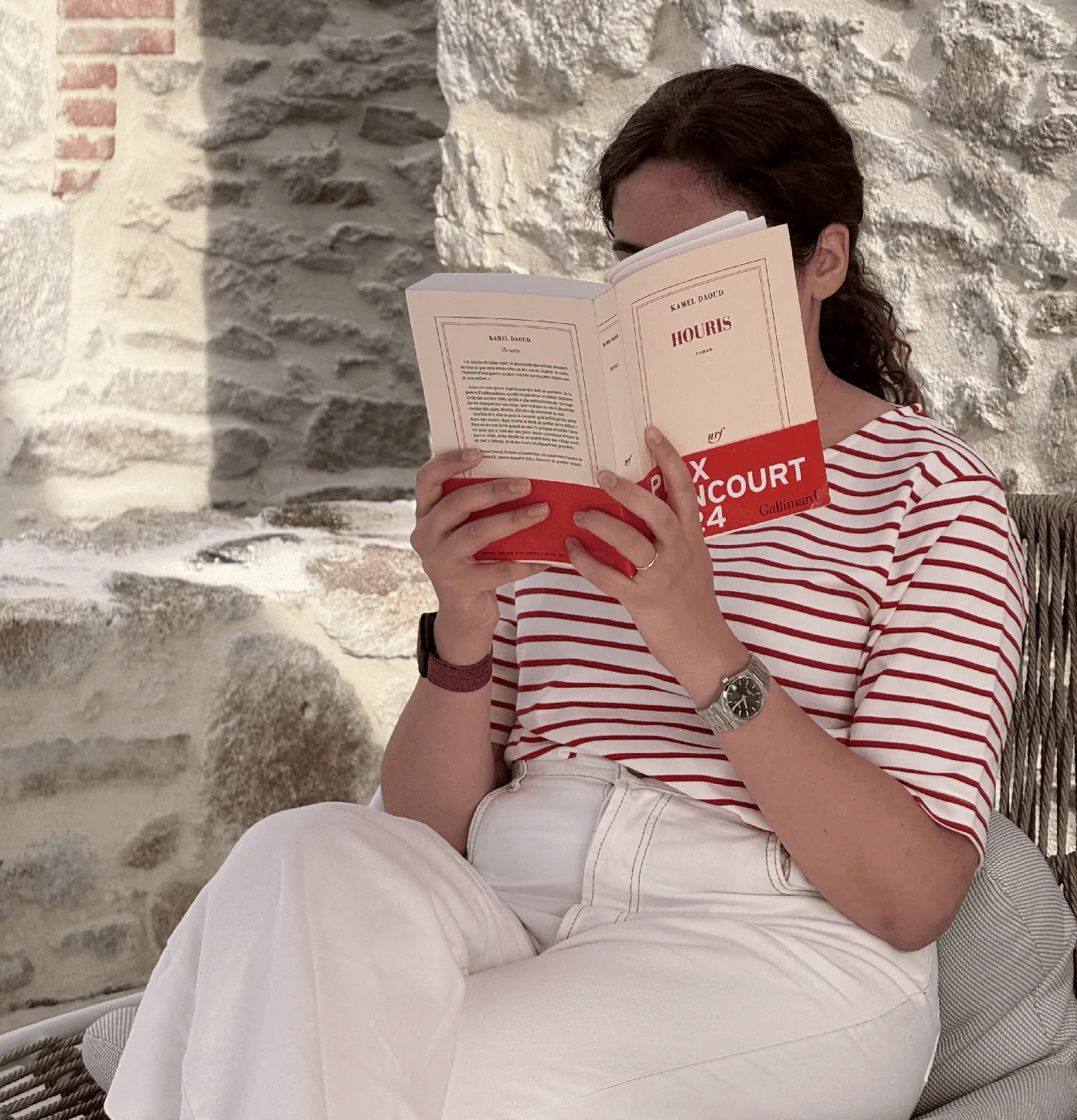 امرأة تقرأ كتابًا أمام جدار حجري